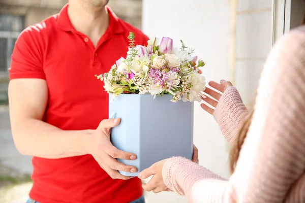 Mujer joven que recibe hermosas flores de entrega hombre en casa — Foto de Stock