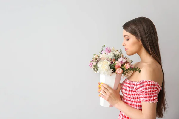 Vacker ung kvinna med bukett blommor på ljus bakgrund — Stockfoto