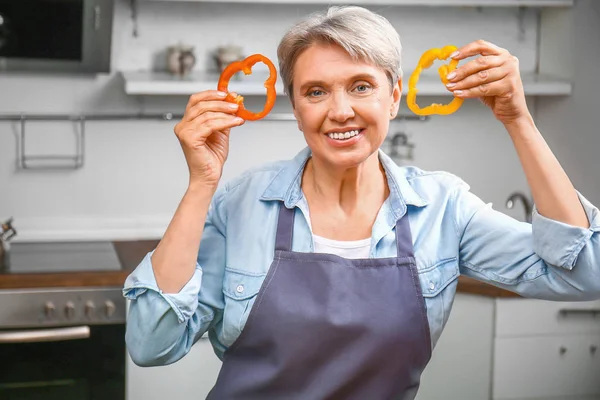 Mulher madura com pedaços de pimenta na cozinha — Fotografia de Stock