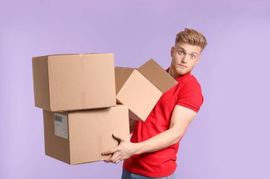 Young man with cardboard boxes on color background