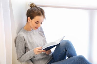 Pencere yakınında kitap okuyan güzel genç kadın