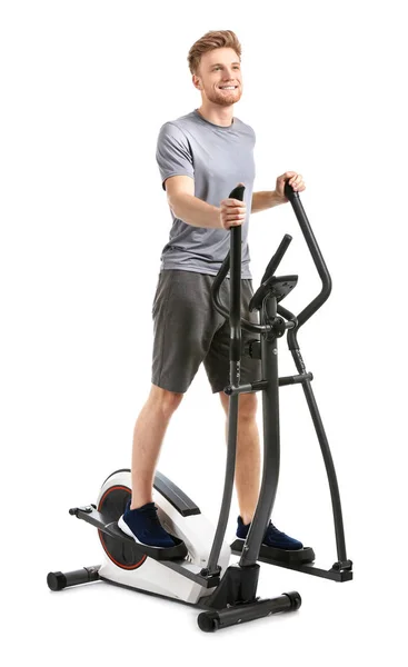 Sporty young man training on machine against white background — Stock Photo, Image