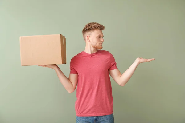 Young man with cardboard box on color background — Stock Photo, Image
