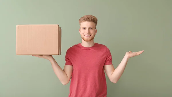 Young man with cardboard box on color background — Stock Photo, Image