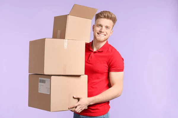 Young man with cardboard boxes on color background — Stok fotoğraf