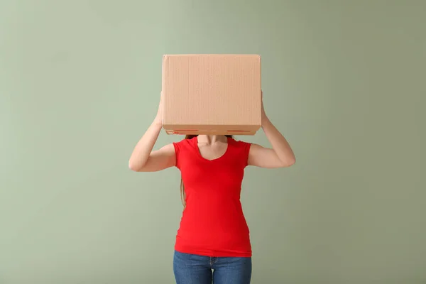 Young woman with cardboard box on color background — Stok fotoğraf