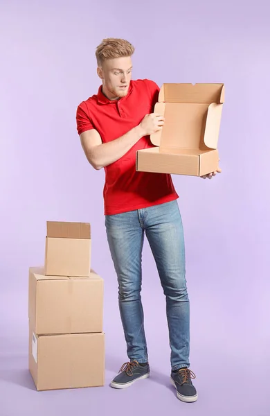 Young man with cardboard boxes on color background — Stok fotoğraf