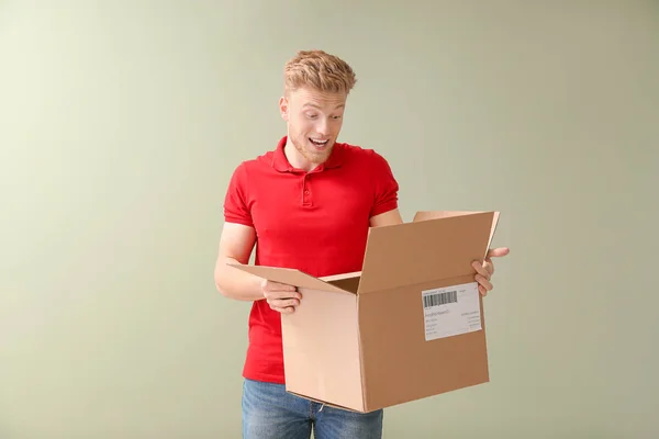 Surprised young man with cardboard box on color background — Stock Photo, Image