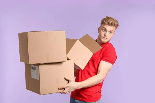 Young man with cardboard boxes on color background — Stock Photo, Image