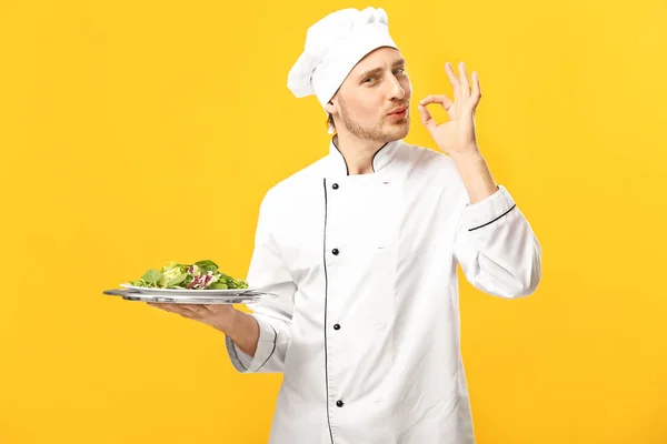 Schöner männlicher Koch mit Salat auf farbigem Hintergrund — Stockfoto