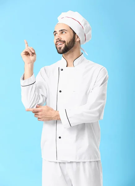 Schöner männlicher Koch mit erhobenem Zeigefinger auf farbigem Hintergrund — Stockfoto