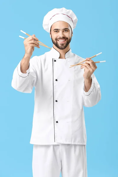 Schöner männlicher Koch mit Essstäbchen auf farbigem Hintergrund — Stockfoto