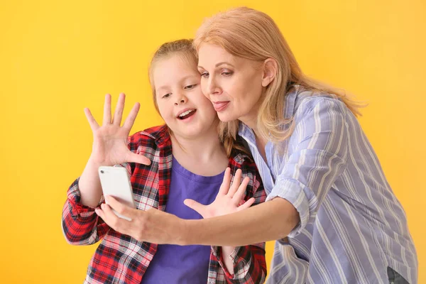 Mature woman and her cute granddaughter taking selfie on color background — Stock Photo, Image