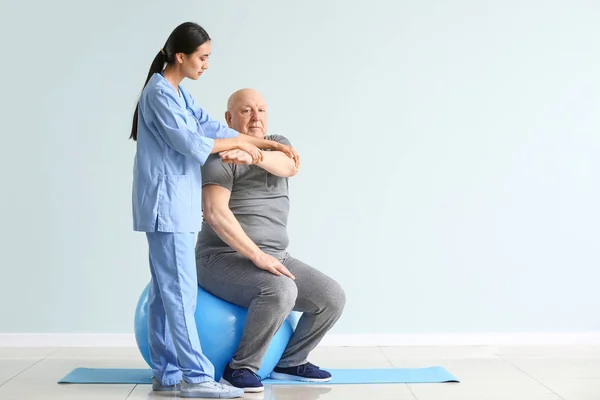Giovane fisioterapista asiatico che lavora con l'uomo anziano in clinica — Foto Stock