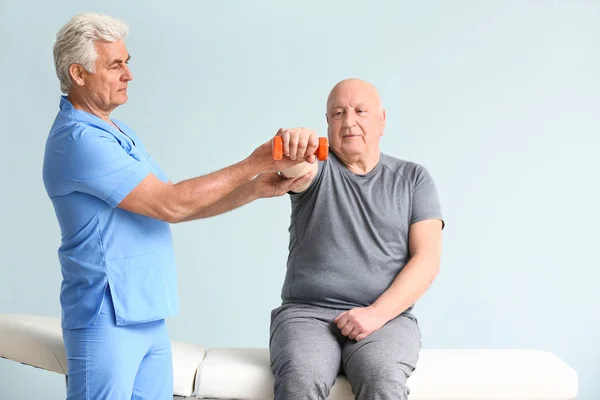 Mature physiotherapist working with senior man on light background — Stock Photo, Image