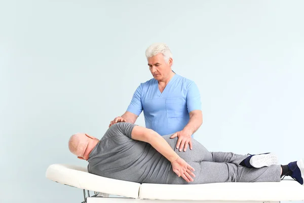 Mature physiotherapist working with senior man on light background — Stock Photo, Image