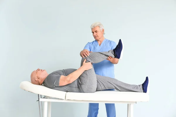 Mature physiotherapist working with senior man on light background