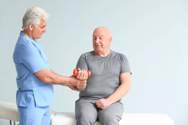 Ältere Physiotherapeutin arbeitet mit älteren Mann auf hellem Hintergrund — Stockfoto