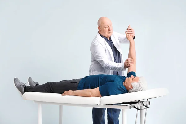 Senior physiotherapist working with mature man on light background