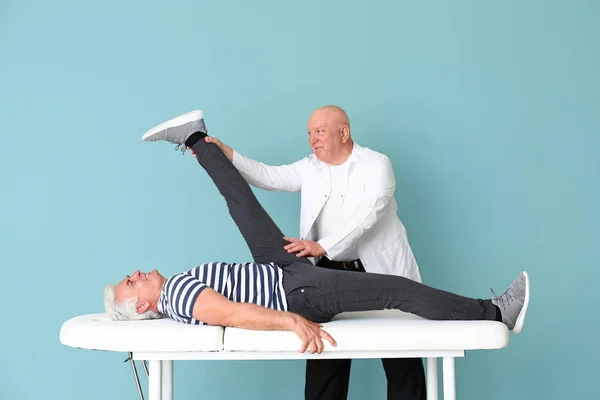 Старший физиотерапевт, работающий со зрелым мужчиной на цветном фоне — стоковое фото