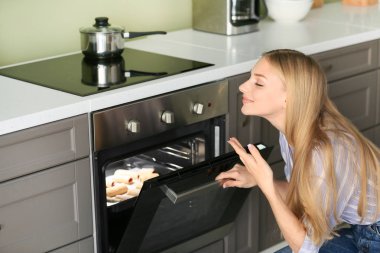 Woman taking baking tray with homemade pastry out of oven