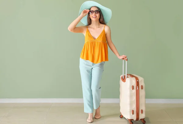 Счастливая молодая женщина с чемоданом возле цветной стены — стоковое фото