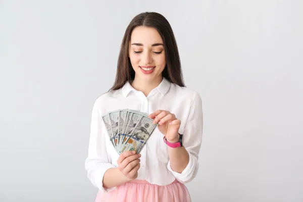 Happy young woman with dollar banknotes on light background — Stock Photo, Image