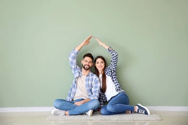 Pareja joven soñando con su nueva casa cerca de la pared de color — Foto de Stock