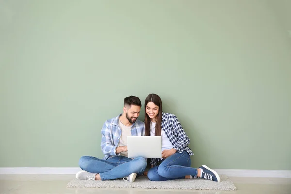 Young couple with laptop sitting near color wall — Stock Photo, Image