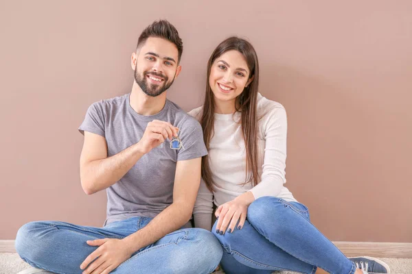 Pareja joven con llaves de su nueva casa sentada cerca de la pared de color — Foto de Stock