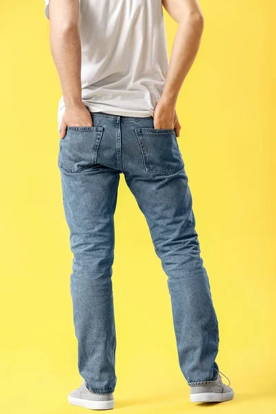 Elegante giovane uomo in jeans su sfondo colore — Foto Stock