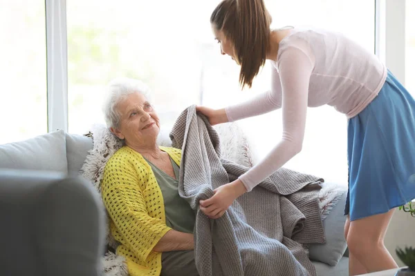 Caregiver covering senior woman with plaid in nursing home — Stock Photo, Image