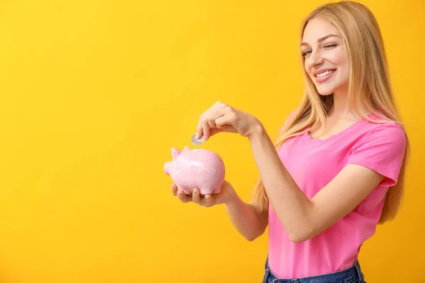 Young woman putting money into piggy bank on color background — Stock Photo, Image