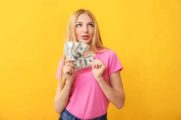 Thoughtful young woman with money on color background — Stock Photo, Image