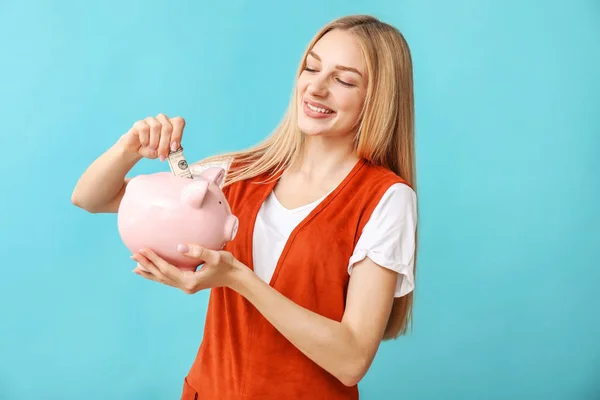 Jovem com banco porquinho no fundo de cor — Fotografia de Stock