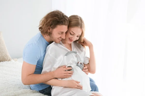 Junges schwangeres Paar mit Kopfhörern zu Hause — Stockfoto