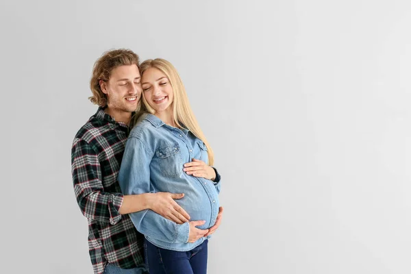 Happy young pregnant couple on light background — Stock Photo, Image