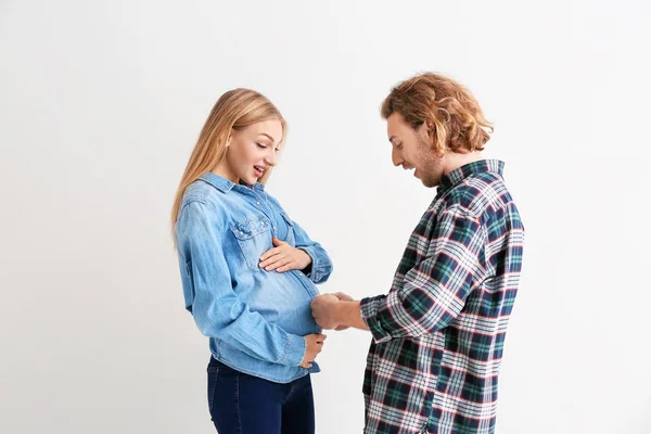 Jonge zwangere vrouw en haar man vergelijken grootte van hun buik op lichte achtergrond — Stockfoto