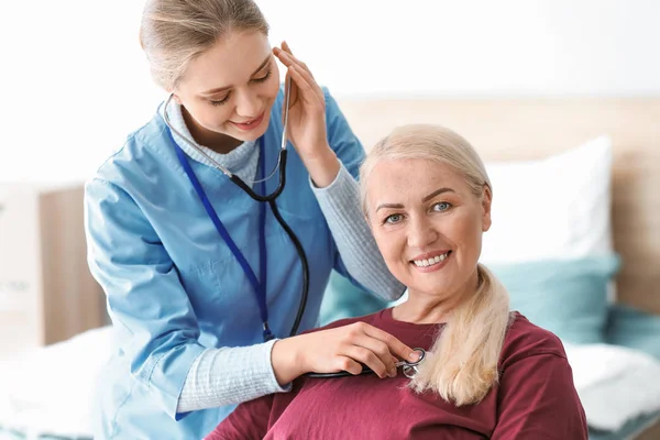 Assistente medico che esamina il paziente maturo con stetoscopio a casa — Foto Stock