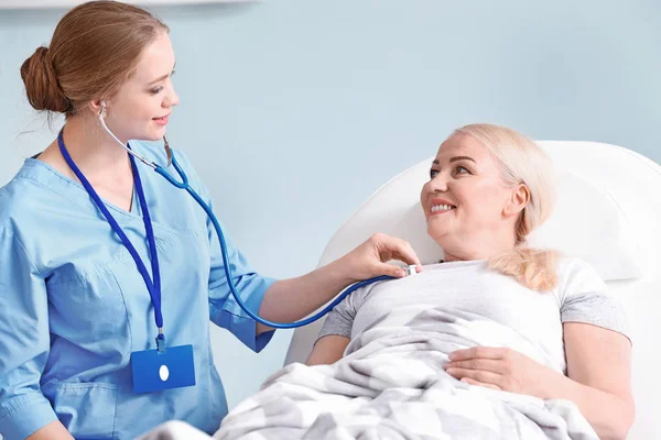 Medical assistant examining mature patient with stethoscope in clinic — Stock Photo, Image