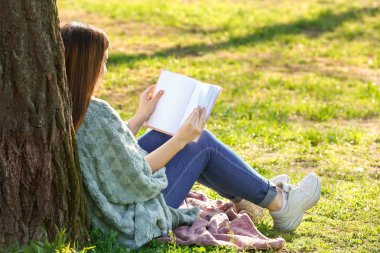 Parkta kitap okuyan güzel genç bir kadın.