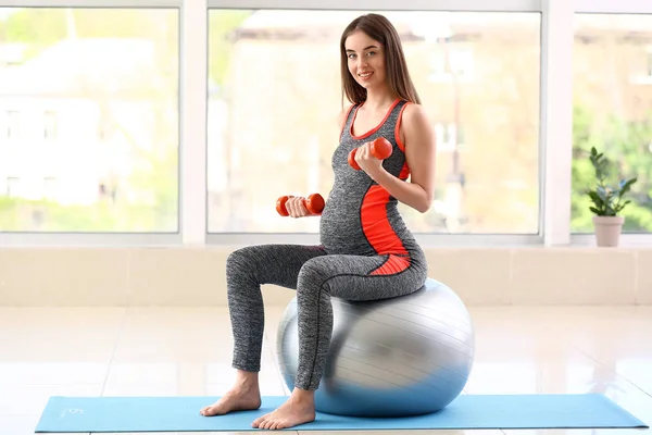 Beautiful pregnant woman with dumbbells and fitball training in gym — Stock Photo, Image