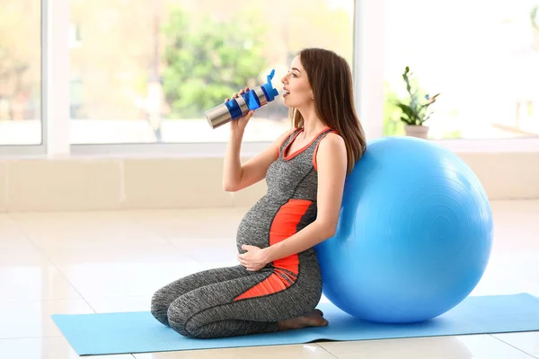 Beautiful pregnant woman drinking water during training in gym — Stock Photo, Image