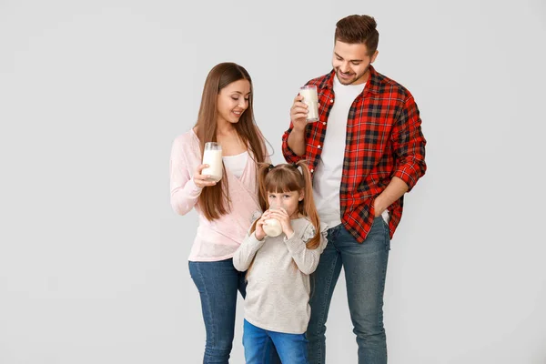 Young family with glasses of tasty milk on light background
