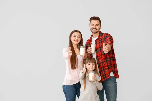 Ung familj med glasögon av välsmakande mjölk visar tummen upp gest på ljus bakgrund — Stockfoto