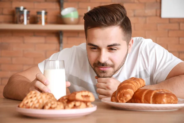 Schöner Mann trinkt leckere Milch mit Bäckerei in Küche zu Hause — Stockfoto