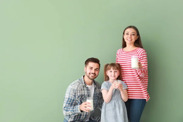 Young family with glasses of tasty milk on color background