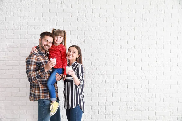 Família jovem com copos de leite saboroso no fundo de tijolo branco — Fotografia de Stock