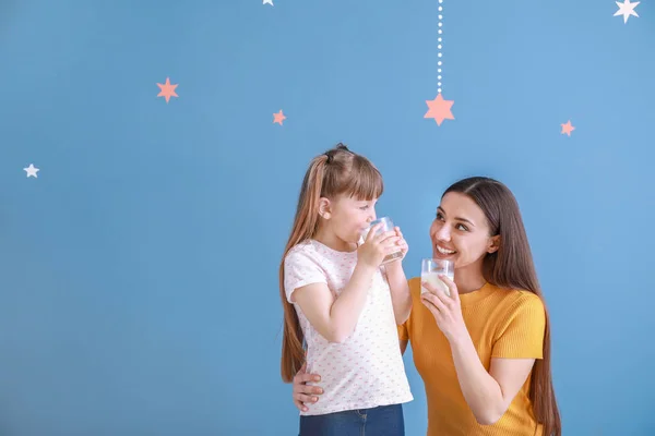 Young mother with little daughter drinking tasty milk on color background — Stock Photo, Image