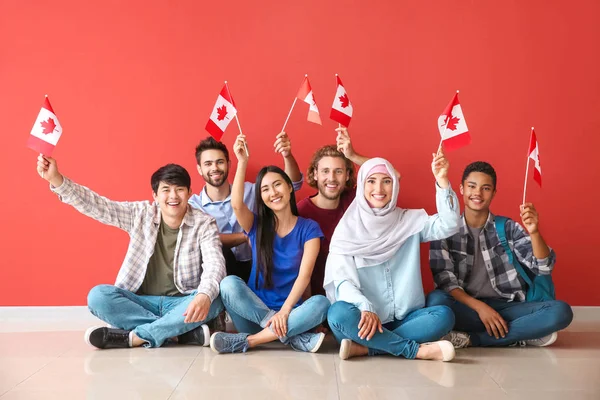 Група студентів з канадськими прапорами сидять біля кольорової стінки — стокове фото